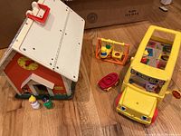Top angle view of the Fisher Price school house with clock above door, moving eye yellow school bus with stop sign, swing set toy with two swinging figures, red wagon, and four small figures outside playsets.
