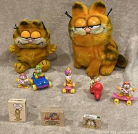 Two vintage Garfield plush toys, four Garfield Happy Meal figurines from 1988, and three Garfield rubber stamps displayed on a neutral background.