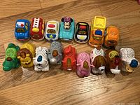 All 16 toys grouped on wooden floor, 9 animal toys and 7 vehicle toys shown