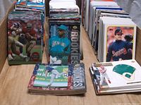 Football and baseball cards displayed standing and stacked in rows, showing a mix of eras and players including rookies and established athletes.
