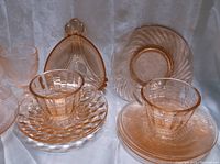 Several pieces of pink glassware including cups, saucers, bowls, and an unusual divided serving dish with handle in soft pink translucent glass.