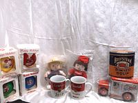 Full view of boxed Campbell's Soup holiday ornaments, two dolls, two ceramic mugs, large Beefsteak Tomato Soup metal tin, and delivery truck tin.