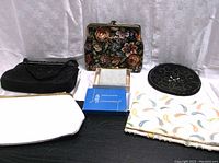Six assorted clutches and coin purses displayed on a dark surface with a white fabric background