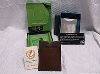 Photo of Tony Perotti leather wallet with original packaging and guarantee card alongside Stewart Stand stainless steel card holder in its box with information card.