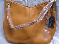 Front view of an amber yellow handbag with pebbled faux leather texture, zippered top, and a shoulder strap covered in plastic wrap to protect it.