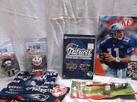 Photo shows two Bleacher Creatures figurines, two fabric pot holders with Patriots and Red Sox logos, a sealed Patriots Super Bowl DVD, a Beckett magazine, and a vintage football action figure.