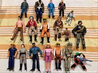 16 assorted action figures arranged on a striped fabric background, showing variety of character styles and clothing