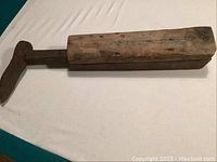 Wooden rectangular base with attached metal shoe form, laying horizontally on a white sheet.