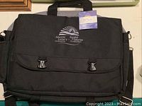 Front view of the black nylon briefcase showing the flap with two clasp closures and the Atlantic Lottery Corporation logo.