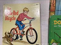 Close-up of The Little Red Bicycle book cover showing illustration of a boy on a red bicycle with a dog following.