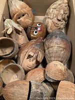 Box containing a mix of natural coconuts and cocoa nuts, some with carved or painted faces