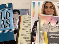 Various magazines, booklets, and printed ephemera including fashion magazines, a calendar, an atlas, and other items spread out on a surface.