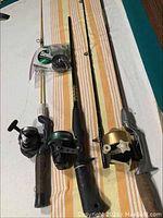 Set of three fishing rods with reels and packaged fishing line on striped fabric background