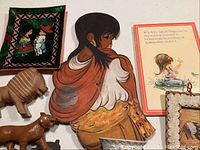 Folk art and decorative items including hand-painted wooden woman wall art, wooden lion figure, greeting card, and framed artwork.