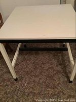 Full frontal view of the table showing the white flat top surface and four metal legs with black accents on feet.
