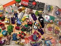 Overview of assortment of vintage toys including cars, animal figurines, Minions characters, Rocket Writers launcher, and packaged Funny Fry Friends figures