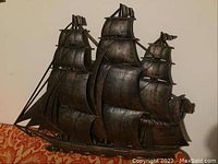 Photo of large dark decorative ship wall sculpture showing three masts and detailed sails and rigging