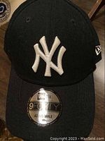Front view of black baseball cap with white NY Yankees embroidery and New Era logo on the side, sticker on visor showing '9FORTY Adjustable'.