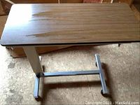 Over bed table showing wood grain laminate top surface and single metal pedestal base with wheels underneath.