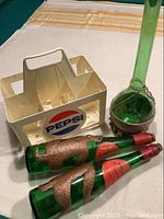 Pepsi plastic carrier with two green glass monkey bottles and tall green glass bottle beside it on fabric surface