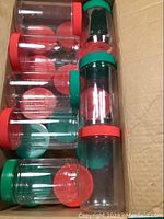 Multiple clear plastic containers with red and green lids stacked in a box.