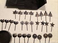 28 themed metal picks in designs of maple leaves, Christmas trees, hearts, snowflakes, stars, apples, and sunflowers arranged next to black round holder.