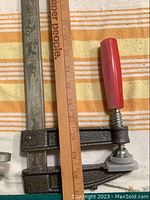 Sliding clamp with red handle laid next to a ruler showing length of about 27.5 inches.