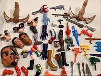 Various toy figure parts including heads, arms, legs, feet, and colorful toy weapons laid out flat