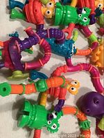 A collection of colorful plastic Twist-A-Zoid toys with flexible segmented limbs and cartoon eyes and faces, tangled and connected in a pile.