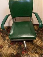Front view of the vintage green leather office chair showing padded armrests and seat.