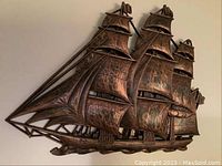 Front view of detailed copper-tone metal wall hanging showing sailing ship with three masts and sails.