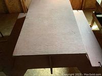 Full view of rectangular wooden picnic table with two benches in a dimly lit room, showing overall shape and condition.