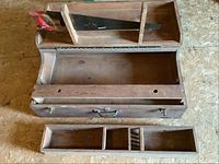 Top view of the open wood toolbox showing one hand saw stored and one large compartment with two removable drawers in front.