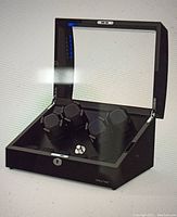 Open black Triple Tree watch winder displaying three rotating watch holders inside a glass-topped case.