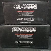 Two black boxes of car cameras stacked, showing 'CAR CAMERA DRIVING VIDEO RECORDER' text and icon features on the packaging.