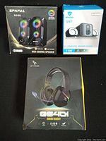 Boxes of two computer speakers and gaming headset showing front packaging with brand and model info.