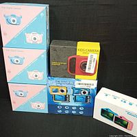 Six kids digital cameras in their original packaging, showing a variety of styles including blue and pink bunny designs, red and dual screen waterproof cameras.