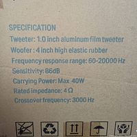 Photo of the speaker specifications printed on packaging showing technical details like tweeter size, woofer size, frequency response, sensitivity, power, impedance, and crossover frequency.