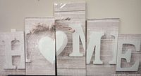Five-panel canvas print spelling HOME with a heart for O in white distressed letters on rustic wood background.