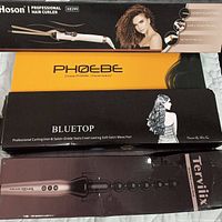 Photo of all three curling irons' packaging boxes stacked: Hoson X8399, Phoebe Bluetop, Terviiix Spiral Wrap wand.