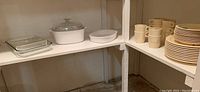 Wide view showing bakeware on lower shelf and Melmac mugs and plates on upper shelf in basement storage