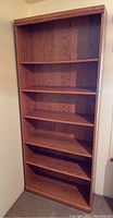Front view of the tall wooden bookcase showing all five shelves and back panel, highlighting size and wood grain.
