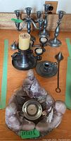 Photo showing an assortment of pewter candleholders including a five-arm candelabra, single holders, one with a candle inserted, along with two metal candle snuffers and loose candles on a surface.