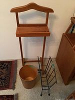 Wood clothes butler, teak waste paper bin, and metal magazine rack set shown from front, placed on carpet near wall.
