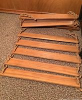 Handmade wooden hanging shelf laid flat showing 9 connected wooden shelves with braided rope sides, detail of rope damage visible on one side.