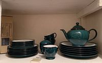 Photo of stacked Denby dinnerware in Greenwich pattern in dark teal with plates, cups, creamer, sugar bowl, and teapot.