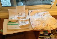 Overview of the entire lot showing folded tablecloth with embroidered floral patterns and lace edging alongside four matching embroidered linen napkins.