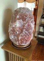 Large natural Himalayan salt lamp on wooden base shown from front angle, highlighting pink and white crystalline texture.