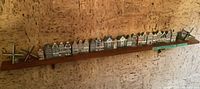 Wide view of all 24 miniature Dutch houses and 4 windmills lined up on a wooden shelf against a textured wall.