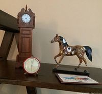 Full view of the Painted Pony figurine next to miniature wooden grandfather clock and Collector's Checklist cards on a wooden shelf.